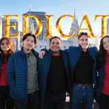 A-group-of-seven-young-adults-smile-at-the-camera-in-front-of-a-cityscape-with-the-word-DEDICATE-superimposed